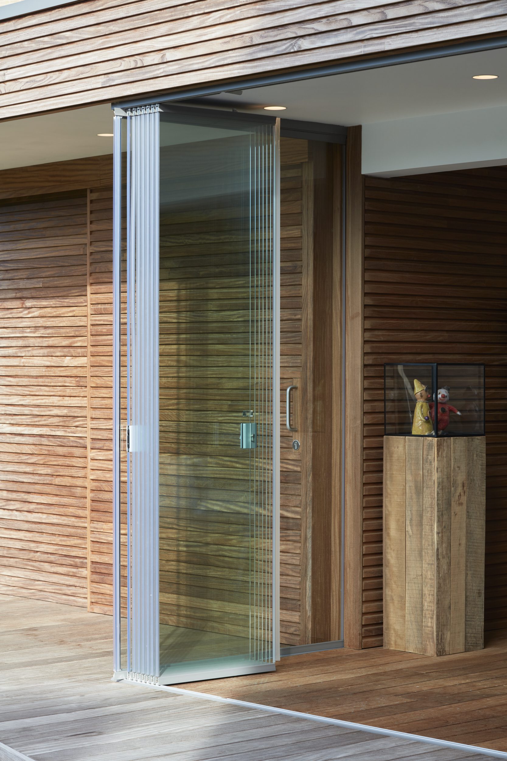 Sliding Glass ONE glazen schuif-draaisysteem met opengevouwen glaspanelen aan moderne houten gevel en terrasvloer