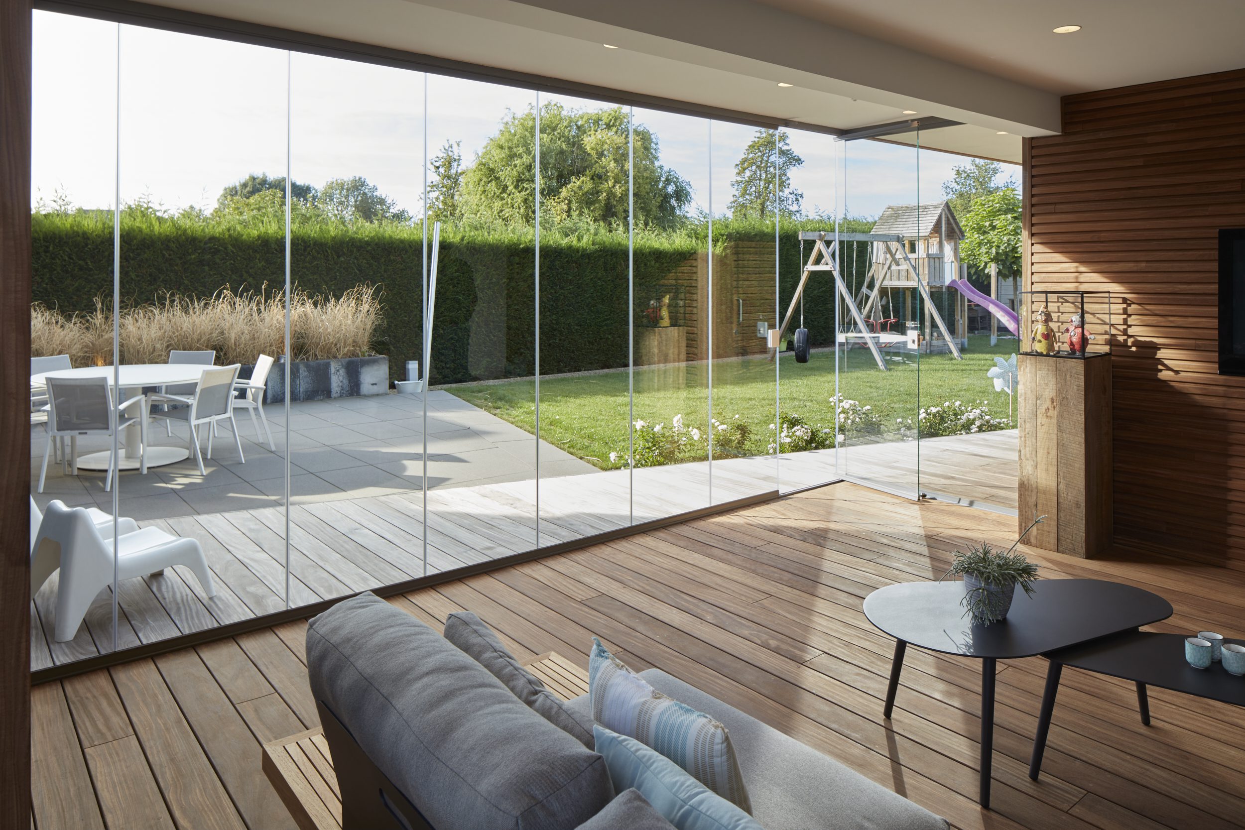 Volledig open tuinzicht vanuit leefruimte met transparante glazen schuifwand en naadloze overgang naar terras en buitenruimte
