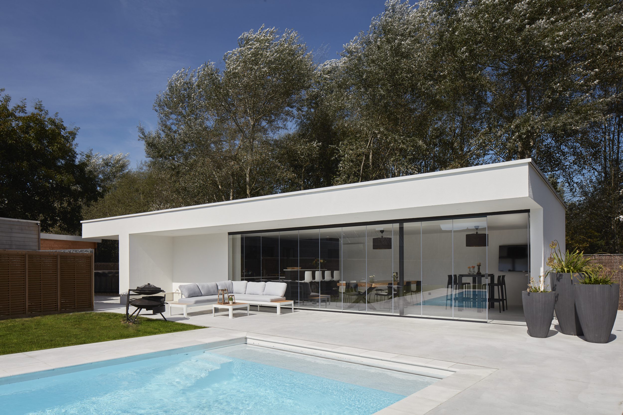 Glazen schuifwand die een modern wit poolhouse afsluit, met naadloze overgang tussen binnen en buiten, gerealiseerd door Sliding Glass