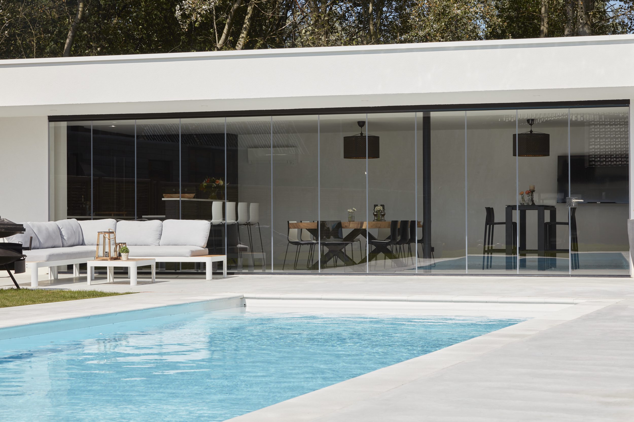 Glazen schuifwand die een modern wit poolhouse afsluit, met naadloze overgang tussen binnen en buiten, gerealiseerd door Sliding Glass