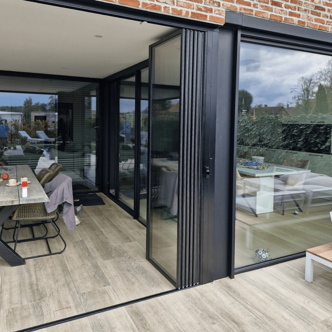 Zwarte schuif-draaiwand op overdekt terras met volledig opengevouwen glaspanelen voor maximale doorgang en zicht op de tuin
