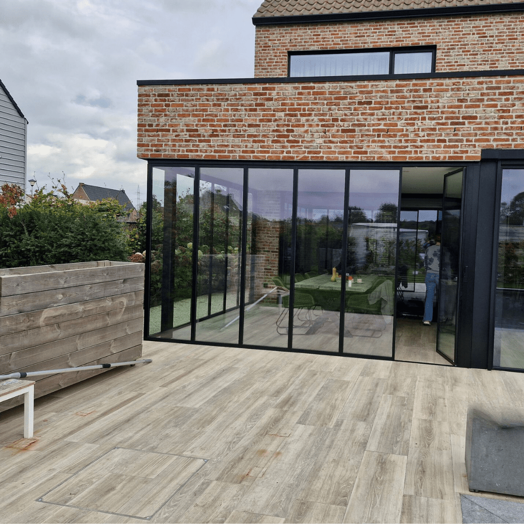 Terrasuitbreiding met zwarte glazen schuifpanelen aan bakstenen woning voor een open verbinding tussen interieur en tuin