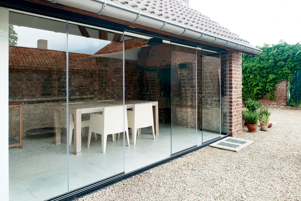 Glazen schuifwand van Sliding Glass in landelijke woning met zicht op binnenkoer, laat veel licht binnen en behoudt het authentieke karakter van de bakstenen gevel