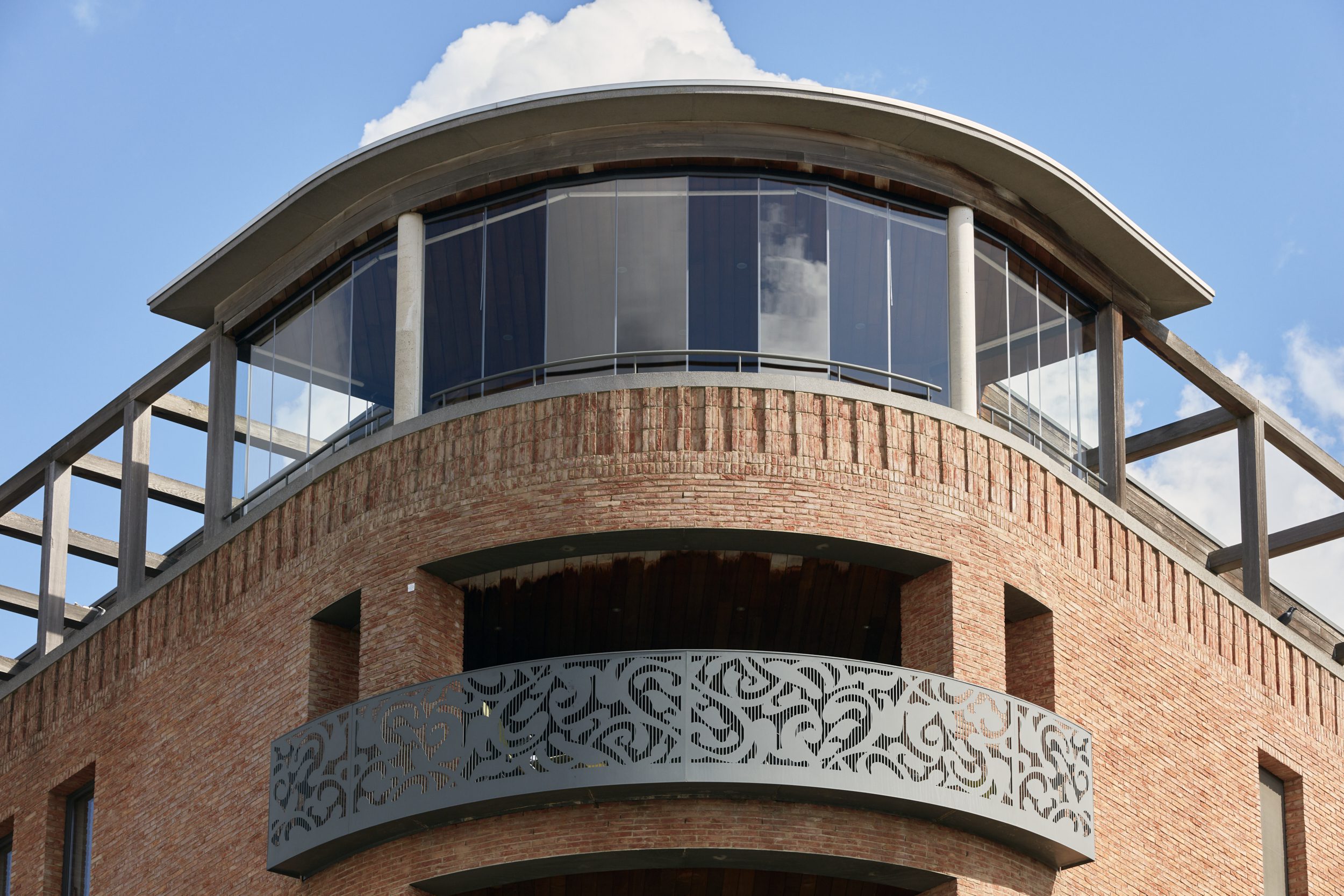 Fraaie glazen schuifwand van Sliding Glass op de bovenverdieping van een modern gebouw met ronde gevel in rode baksteen.