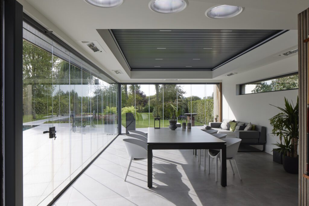 Moderne leefveranda met glazen schuifwanden en open zicht op tuin, terras en zwembad voor maximaal daglicht