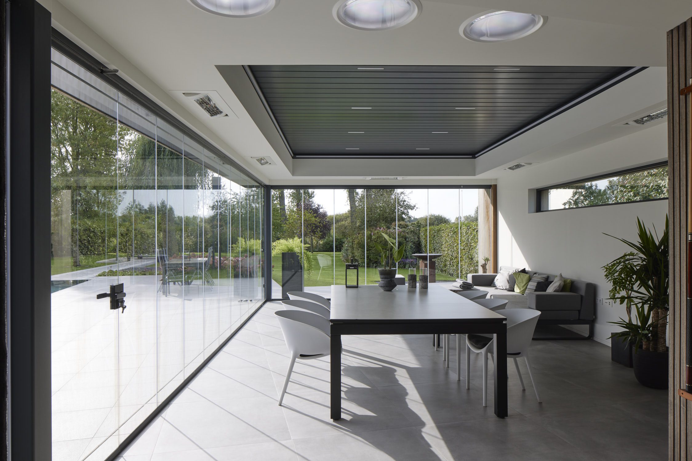 Moderne leefveranda met glazen schuifwanden en open zicht op tuin, terras en zwembad voor maximaal daglicht