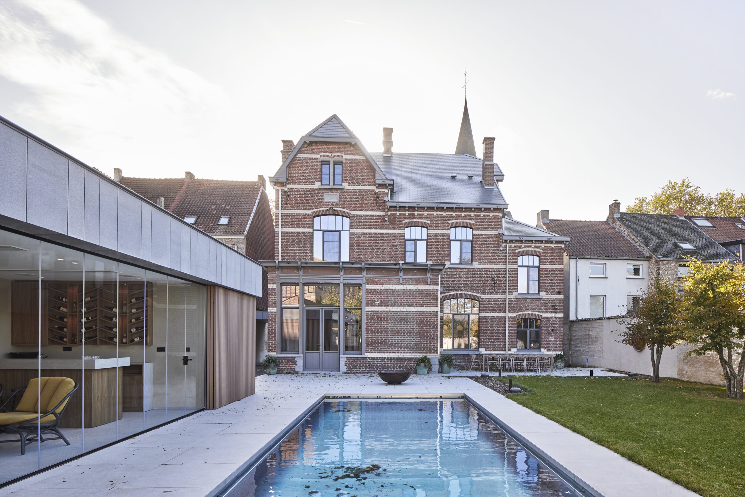 Luxe poolhouse met glazen schuifwanden naast zwembad en karaktervolle villa voor een open zicht en stijlvolle buitenbeleving