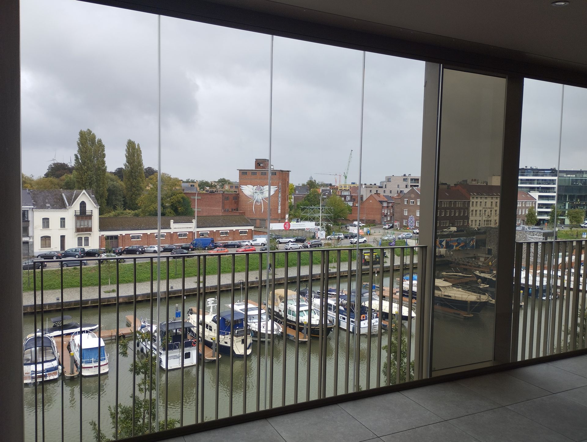 Glazen schuifwand op appartement met uitzicht over jachthaven en stad Hasselt, creëert een open en lichte woonruimte met panoramisch zicht.