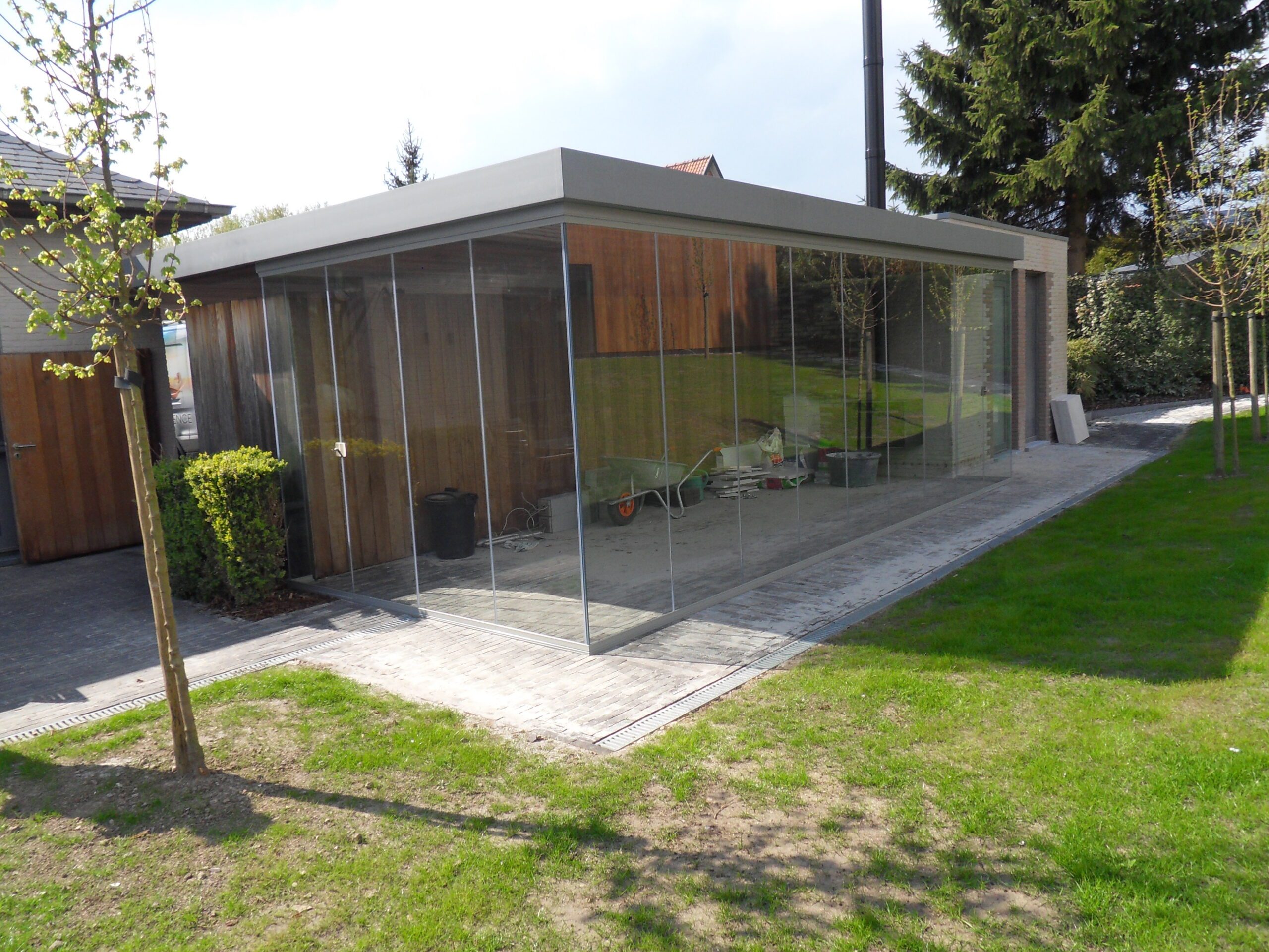 Glazen schuifwanden rondom modern poolhouse met houten gevelbekleding en transparante afsluiting van de tuinruimte