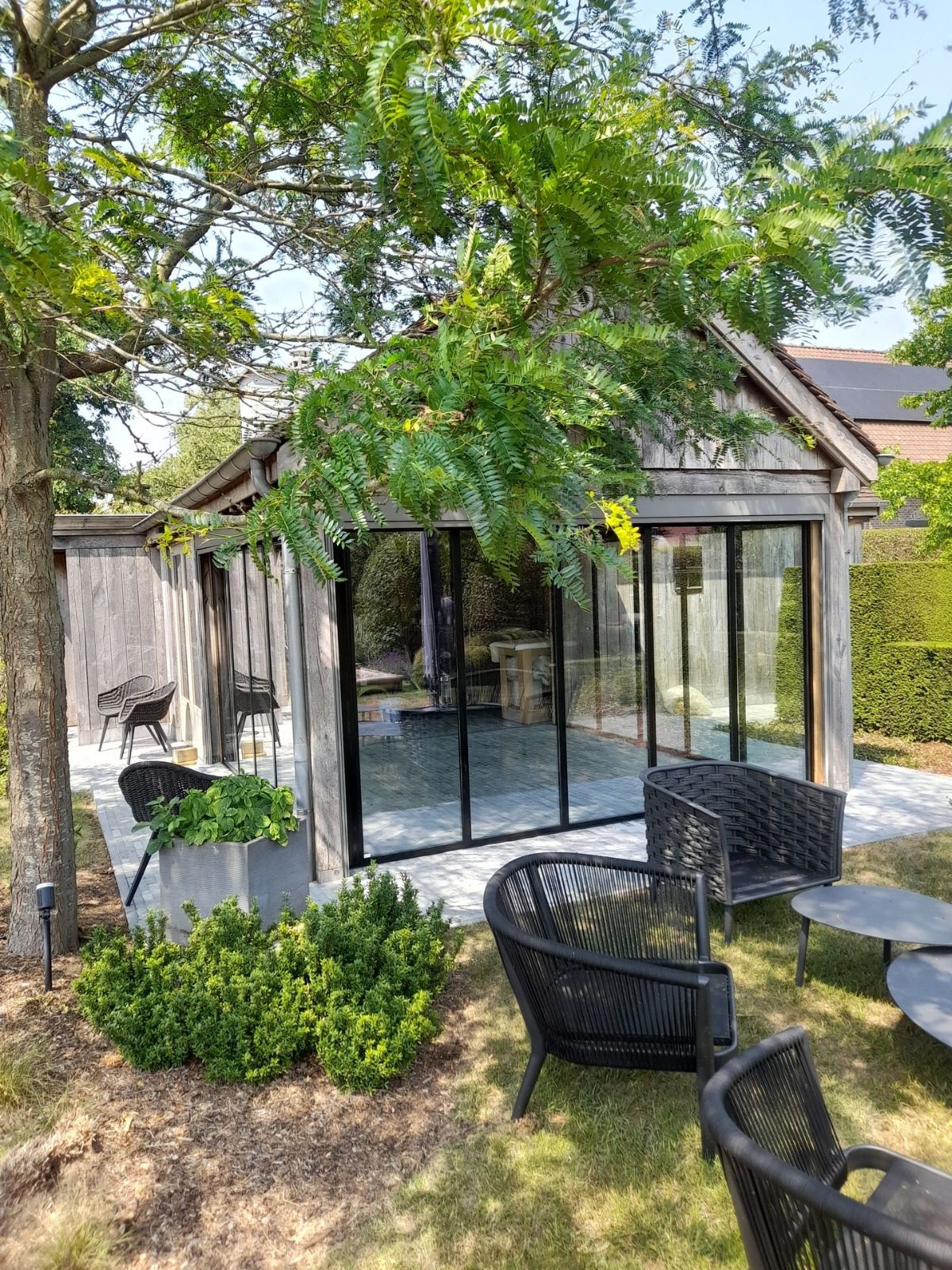 Zwarte glazen schuifwanden in houten poolhouse met landelijke uitstraling en open zicht op tuin en terras